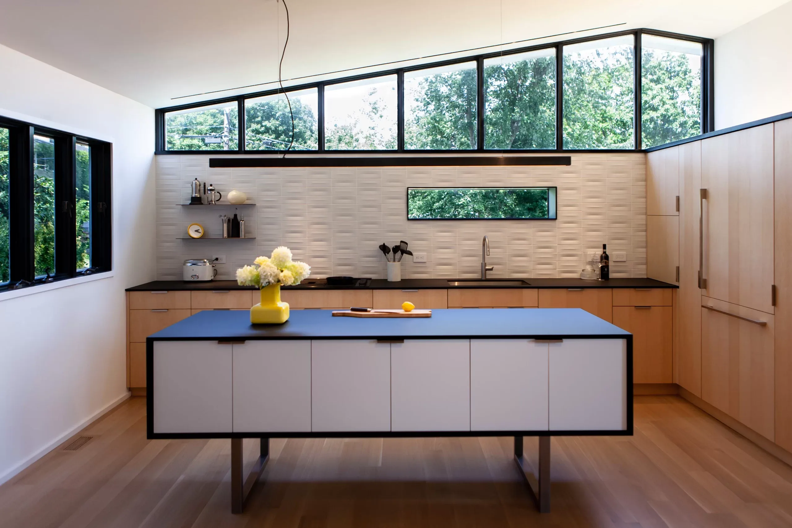 Modern kitchen with floating white island, black countertops, white oak cabinetry, and clerestory windows