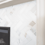 Close-up of a white marble herringbone tile fireplace surround with subtle veining