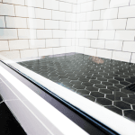 Walk-in shower with black hexagonal floor tiles and white subway tile walls, separated by a glass enclosure