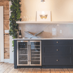 Bar nook with a stainless steel beverage fridge, dark cabinetry, open shelving, and a decorative butterfly print on a marble-look backsplash