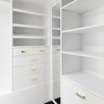 White built-in closet with open shelving, drawers, and gold hardware, including a mirrored door
