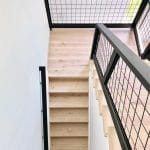 Light wood staircase with black metal railing and wire mesh panels, creating a modern industrial look