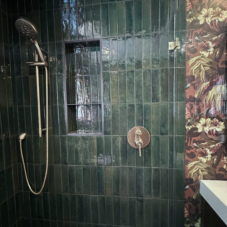 Shower with glossy green vertical tiles, a built-in niche, brass fixtures, and adjacent floral wallpaper
